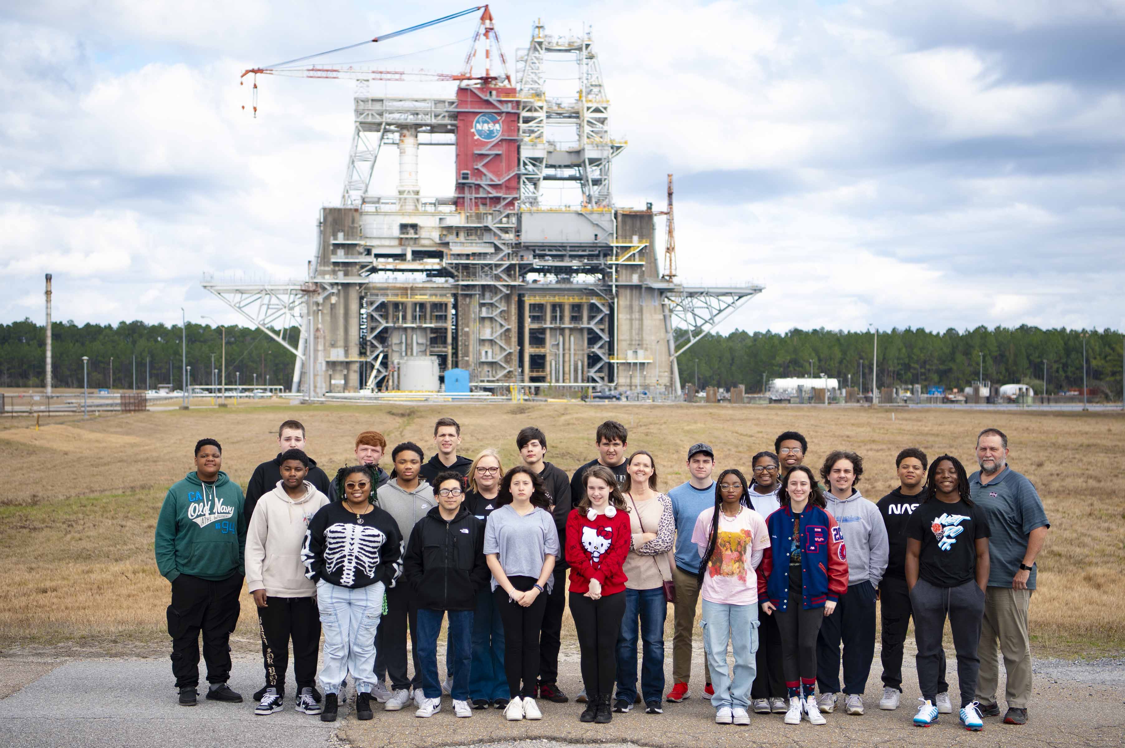 three rows of high school students stand in the forefront with the Thad Cochran Test Stand in the background