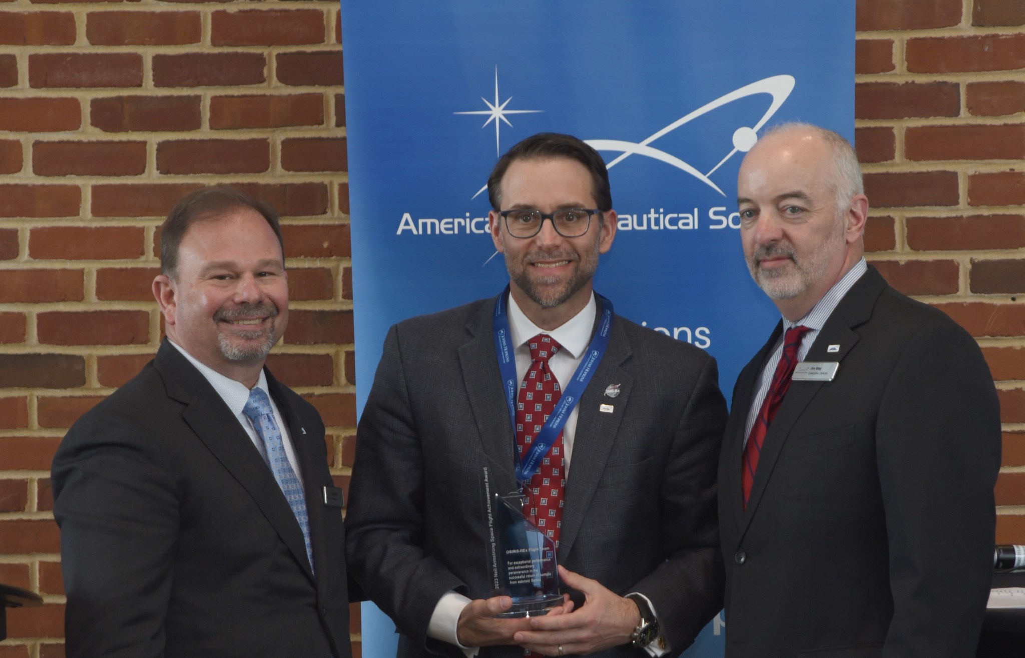 three men in suits in front of a brick wall