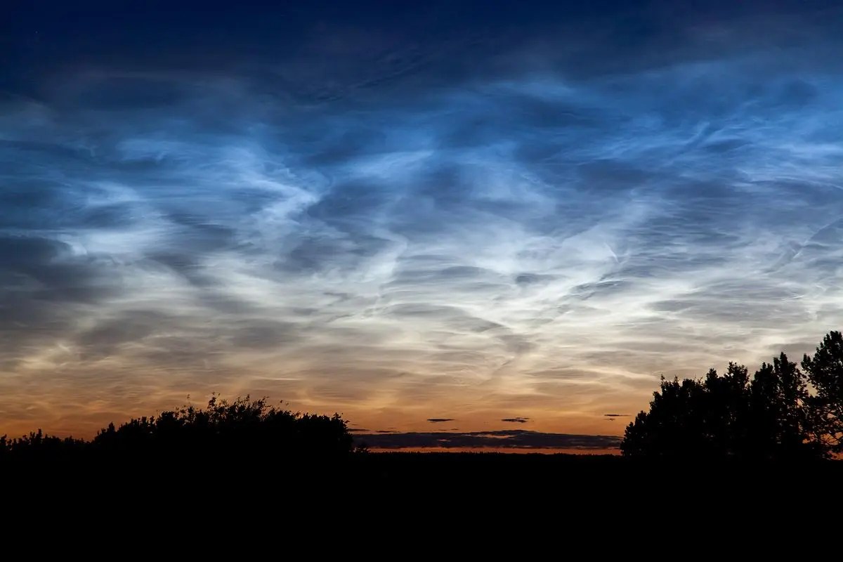 Clouds above a dark landscape appear in the sky. They are