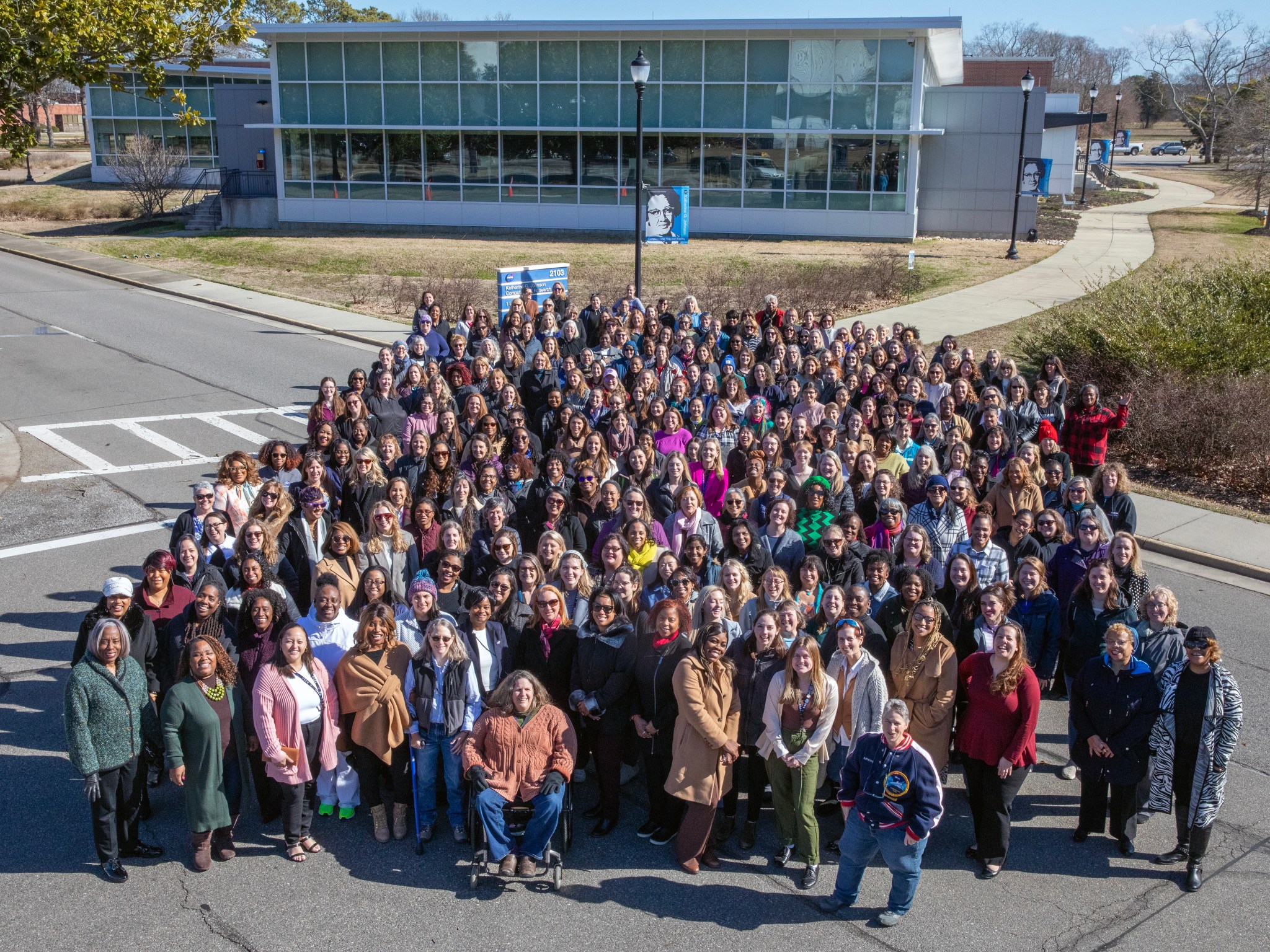 A large group of women gathered for a photo on the street in front of the Katherine G. Johnson Computational Research Facility building.