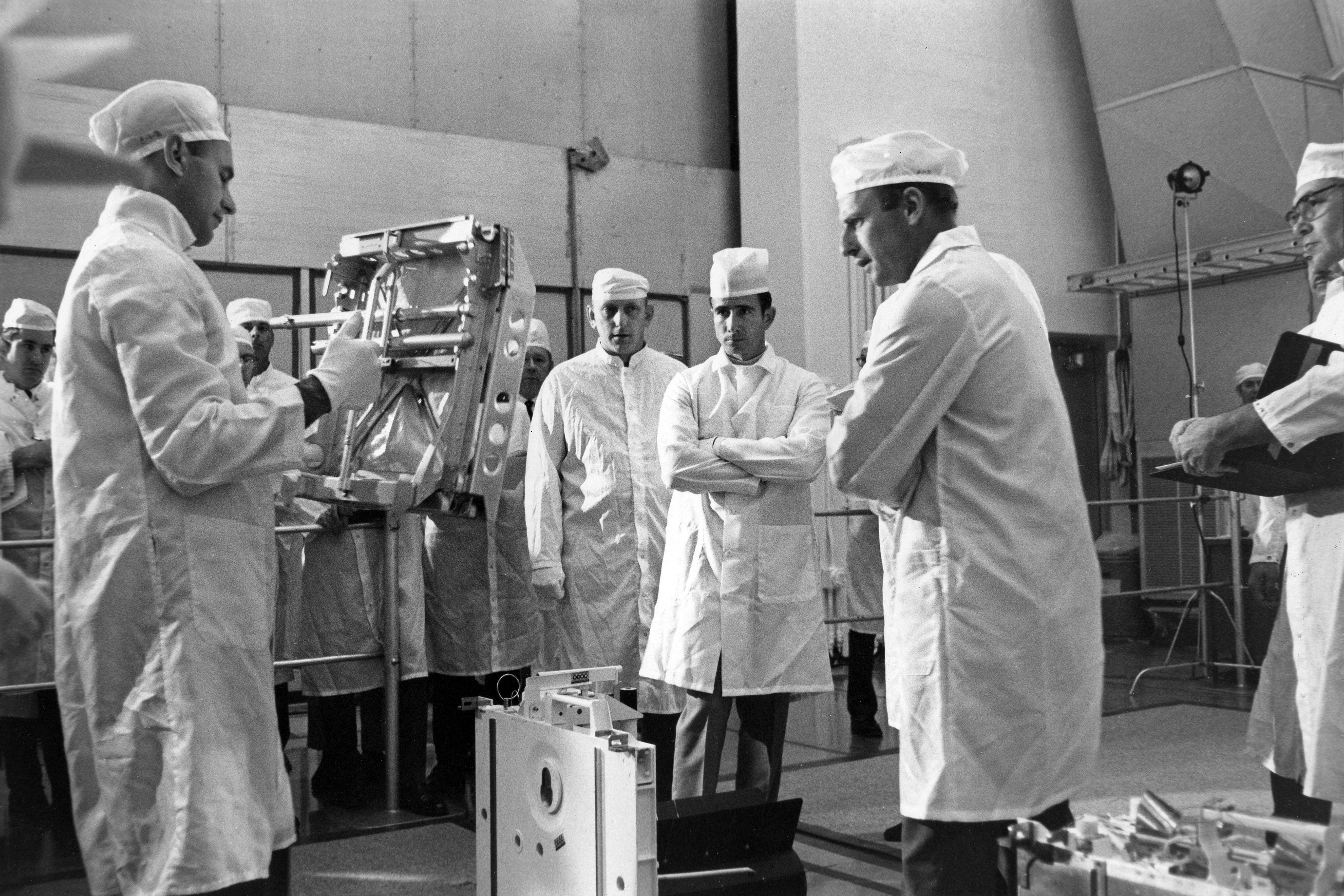 Apollo 12 prime crew members Conrad, left, and Bean, right, review Apollo Lunar Surface Experiment Package equipment as backup astronaut James B. Irwin, with arms folded, looks on