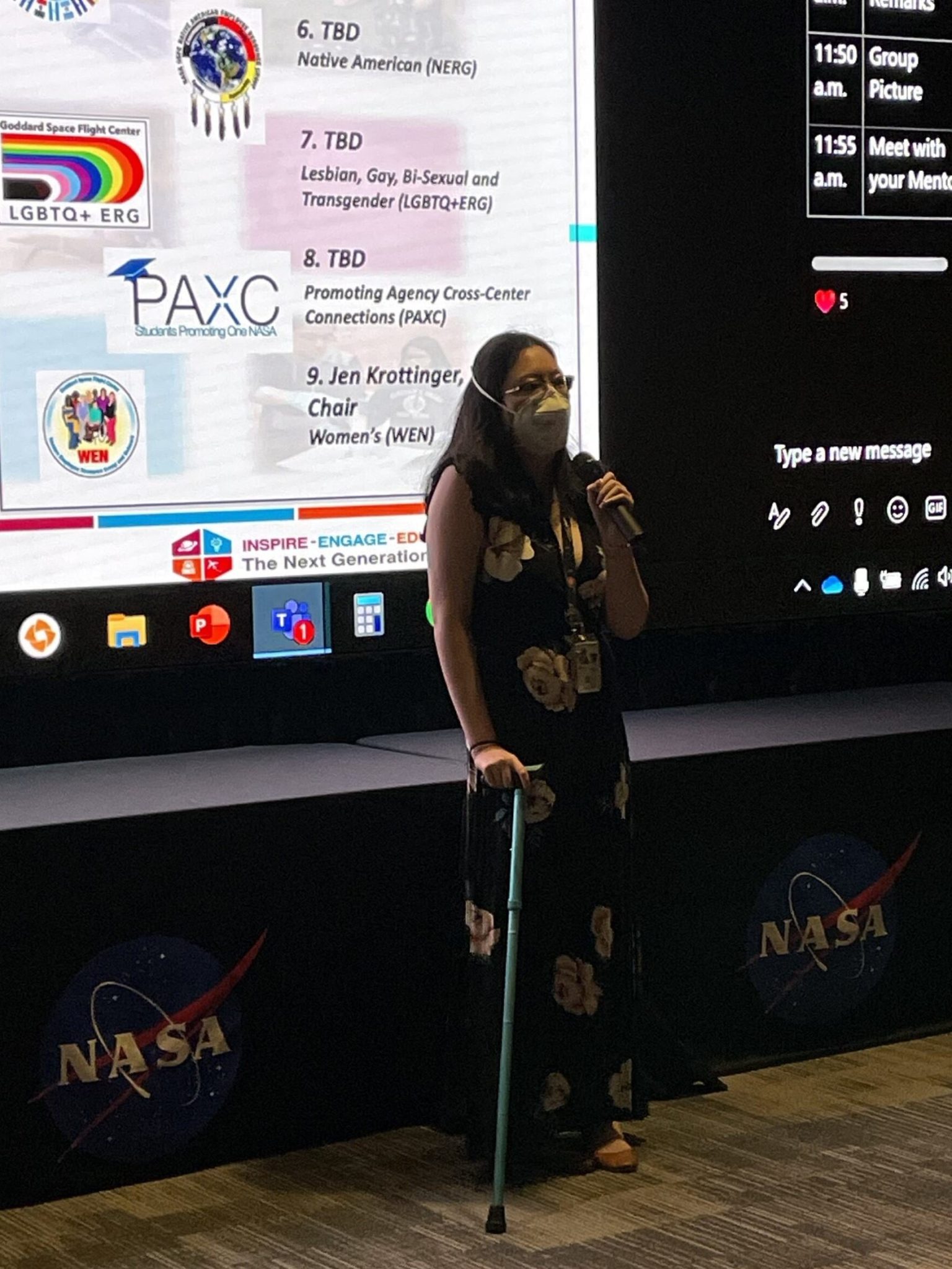  Kiyun Kim speaks in front of a NASA stage with a presentation behind them. They wear a mask and use a blue cane.