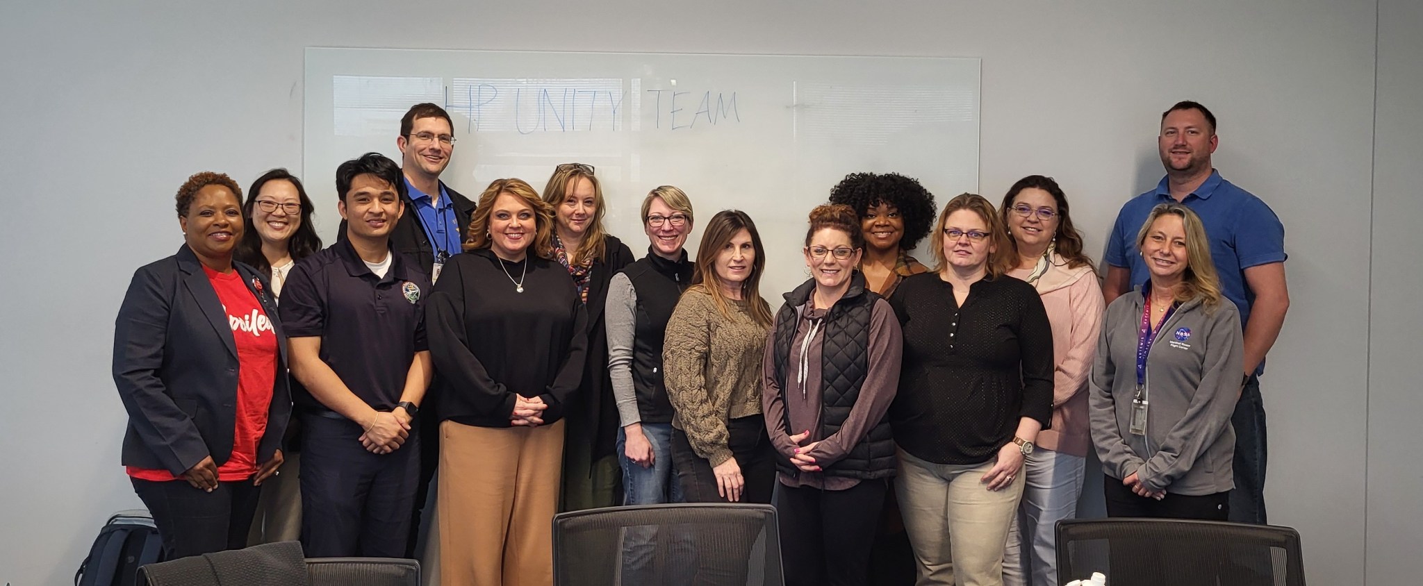 A group of 17 people pose for a photo in front of a grey wall.