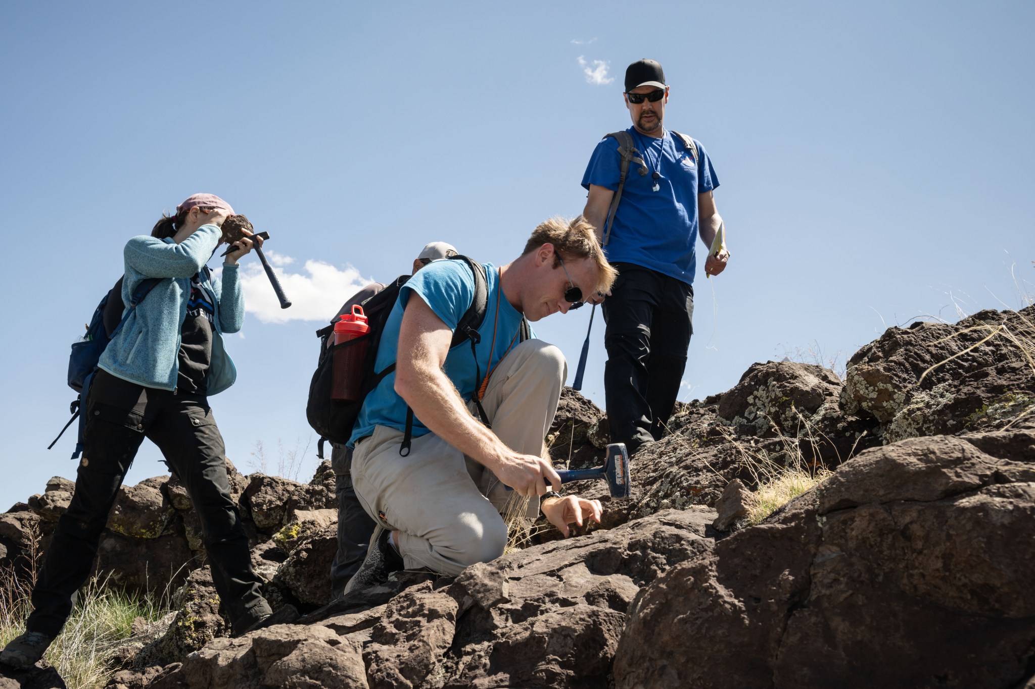 Three people are on a hill made of lava rocks.