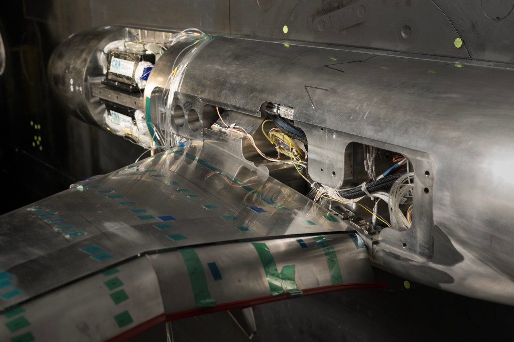 Three compartments of a sliver-colored airplane research model are open and show inside parts and wires of the model.