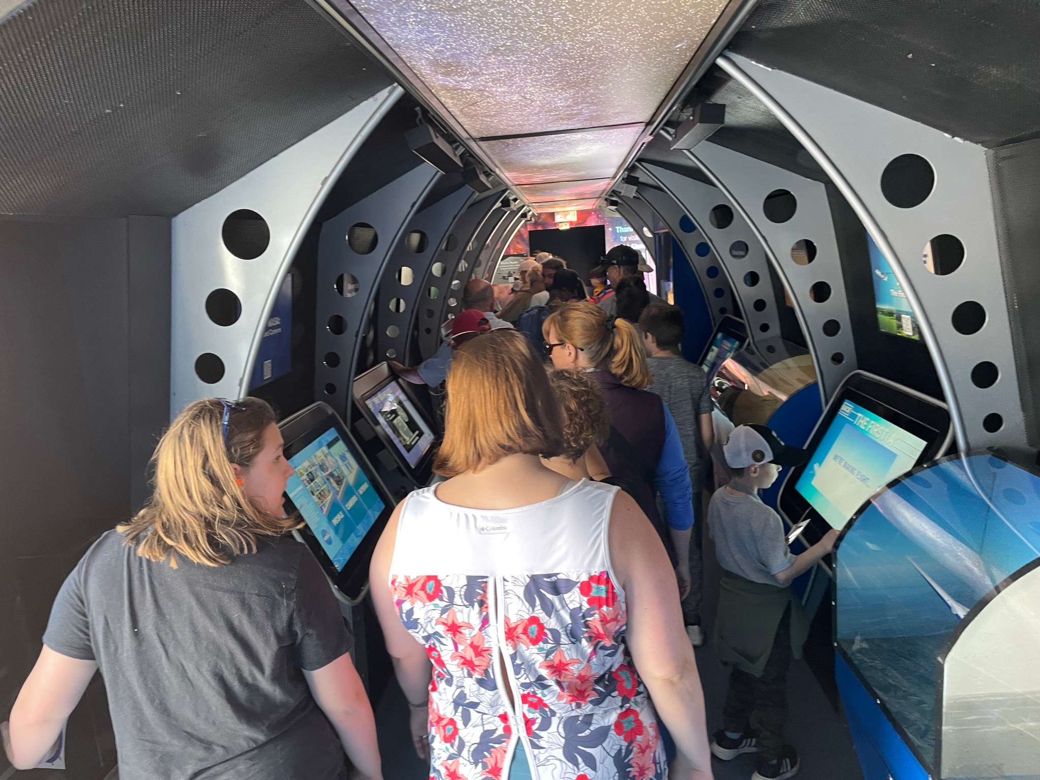 Air show visitors walk through the Journey to Tomorrow traveling exhibit, stopping to look at kiosk screens on both sides of center walkway.