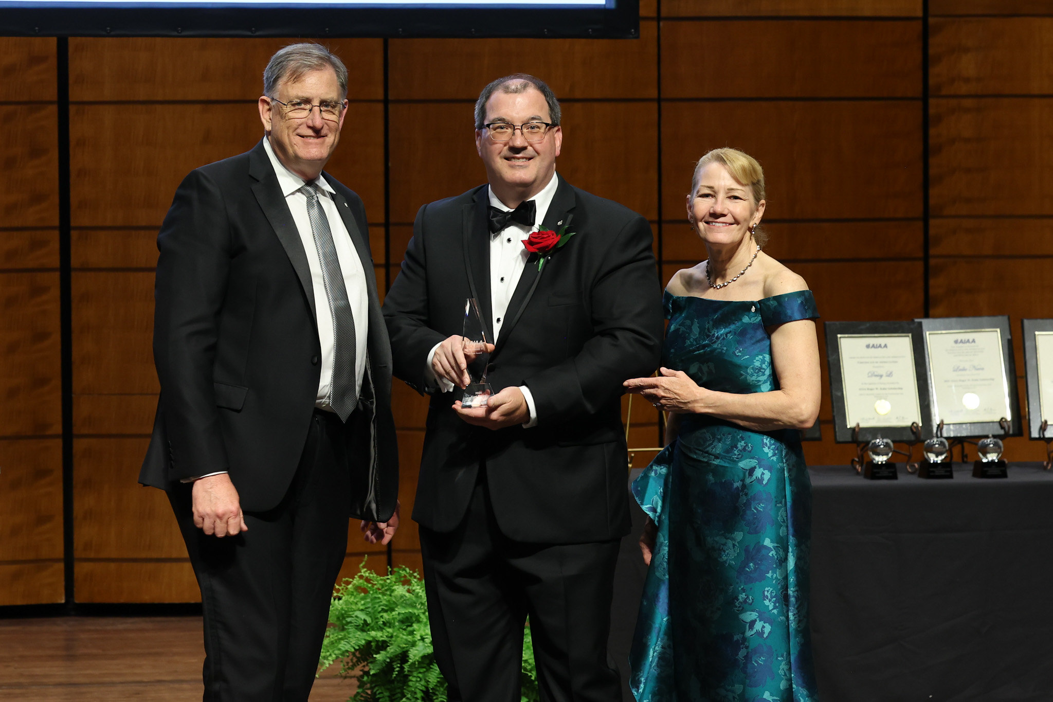 Kurt Polzin, chief engineer for NASA’s Space Nuclear Propulsion Office at the agency’s Marshall Space Flight Center, holds his award between a man and a woman in a green dress.