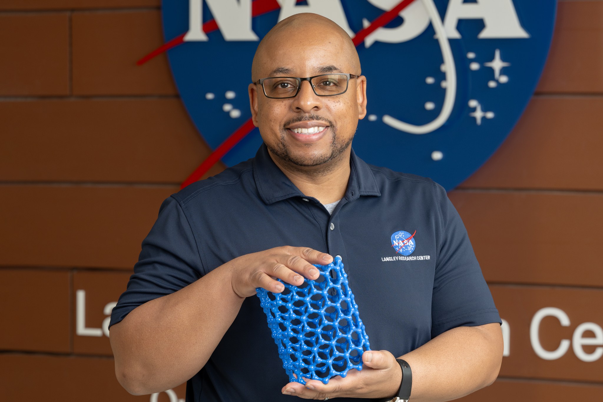 Acting Center Chief Technologist Dr. Phillip A. Williams holds up a model and smiles at the camera. A NASA meatball logo can be seen in the background.