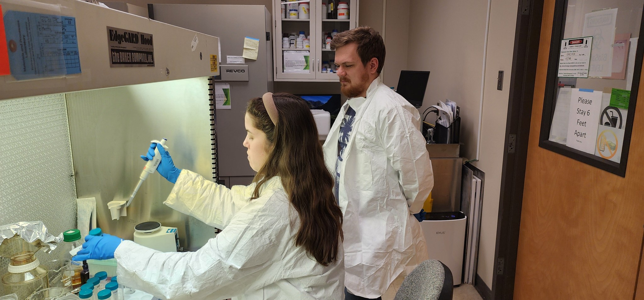 A woman, seated, and a man, standing alongside her, both in lab coats, analyze biofilm samples taken from the test rack at NASA’s Marshall Space Flight Center in Huntsville, Alabama.