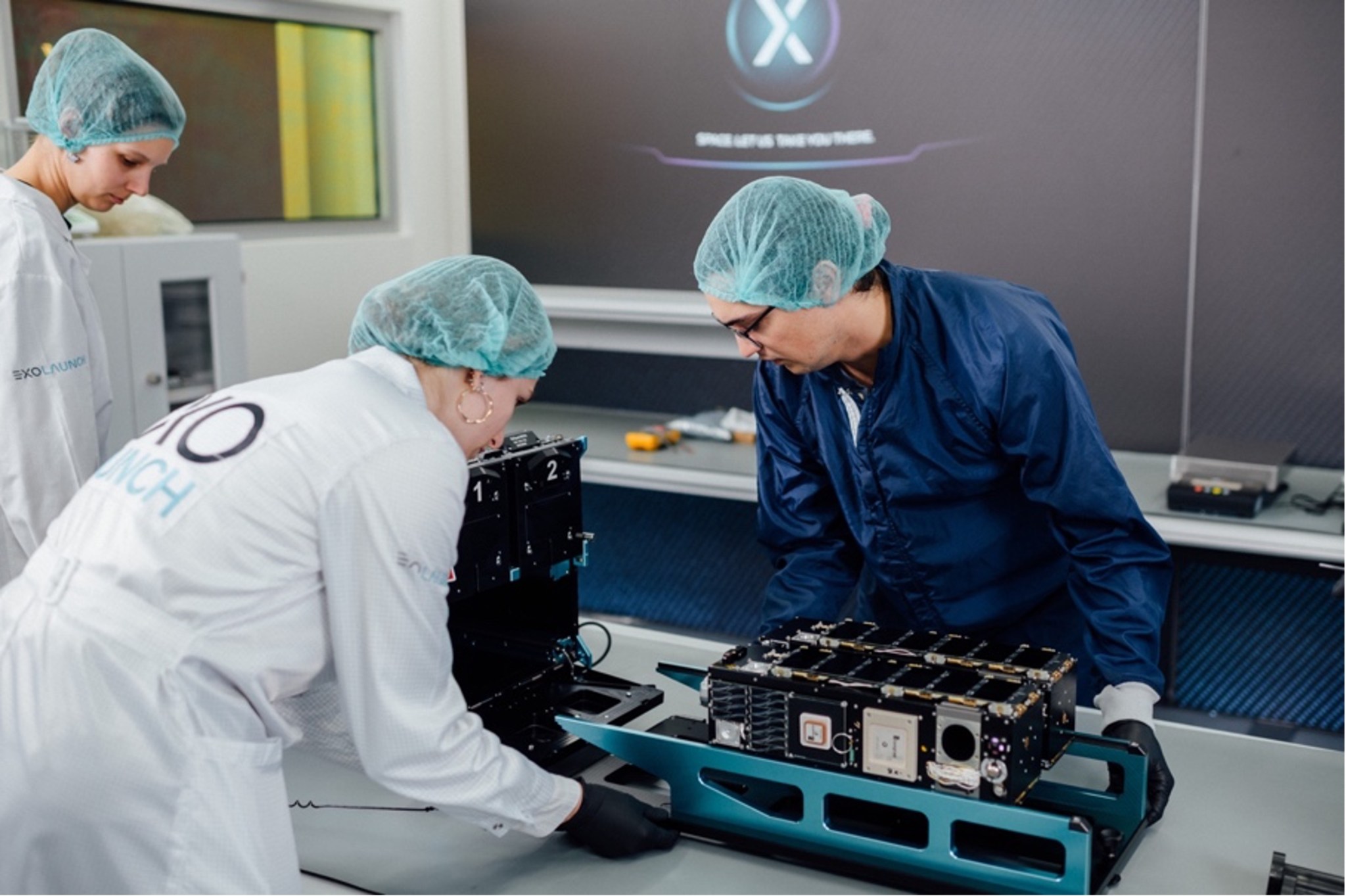 People in hairnets and clean suits connect components with a black box.