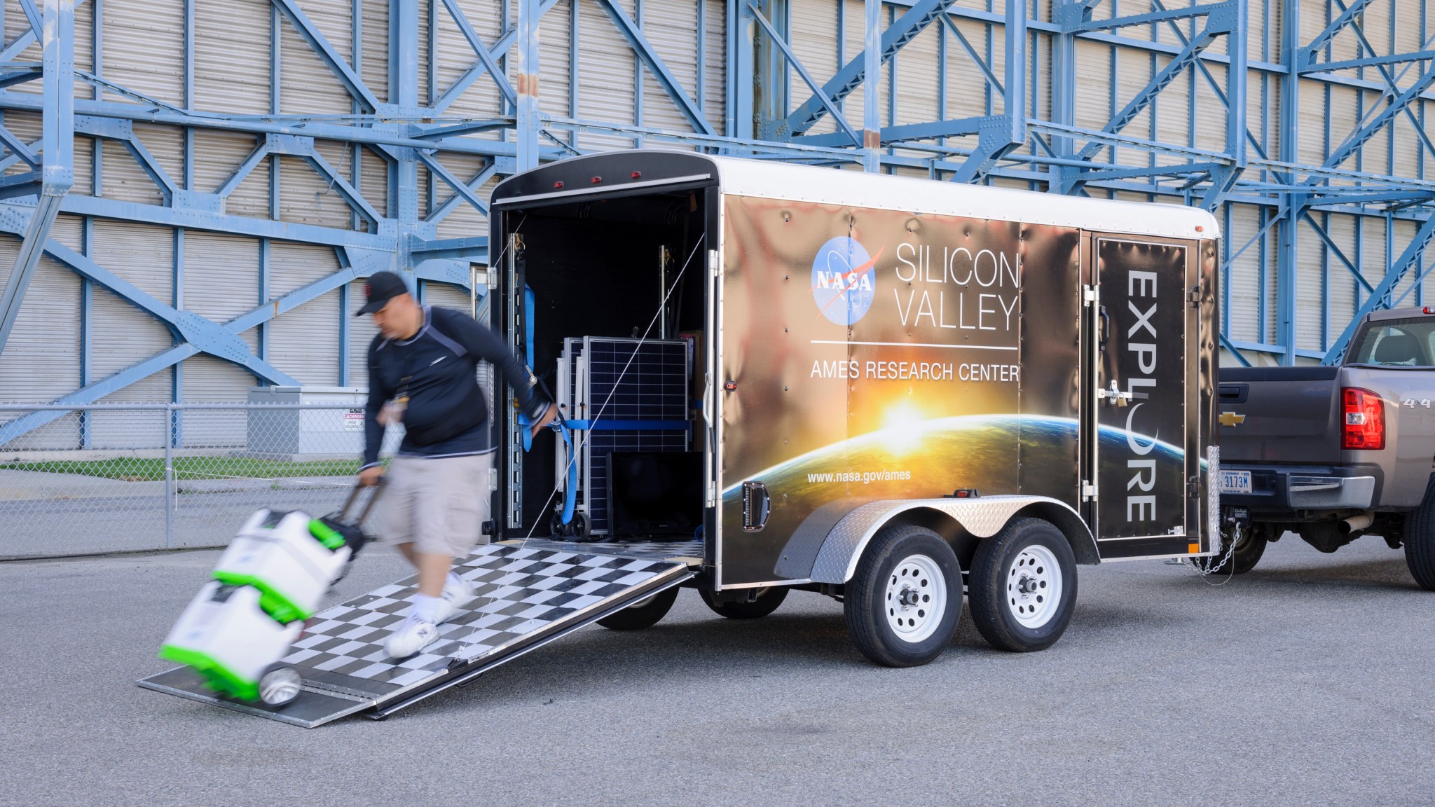 A person rolling a handcart of boxes off the ramp of a small cargo trailer.