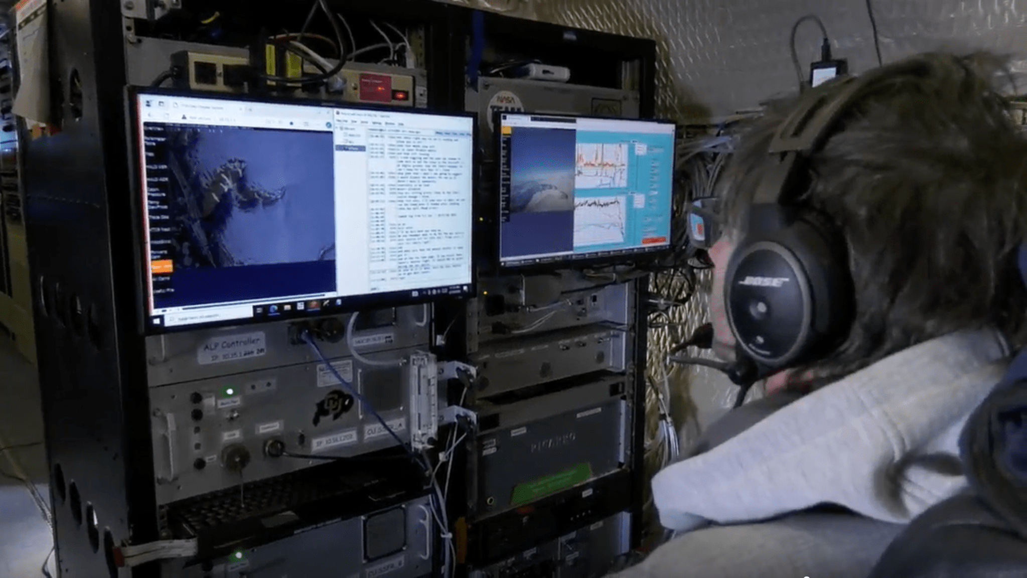 Photo shows the profile of a NASA instrument operator wearing a headset looking at two monitors. The monitors are mounted into an industrial looking equipment rack and show views of the ice covered ground and data measurements along with line graphs.