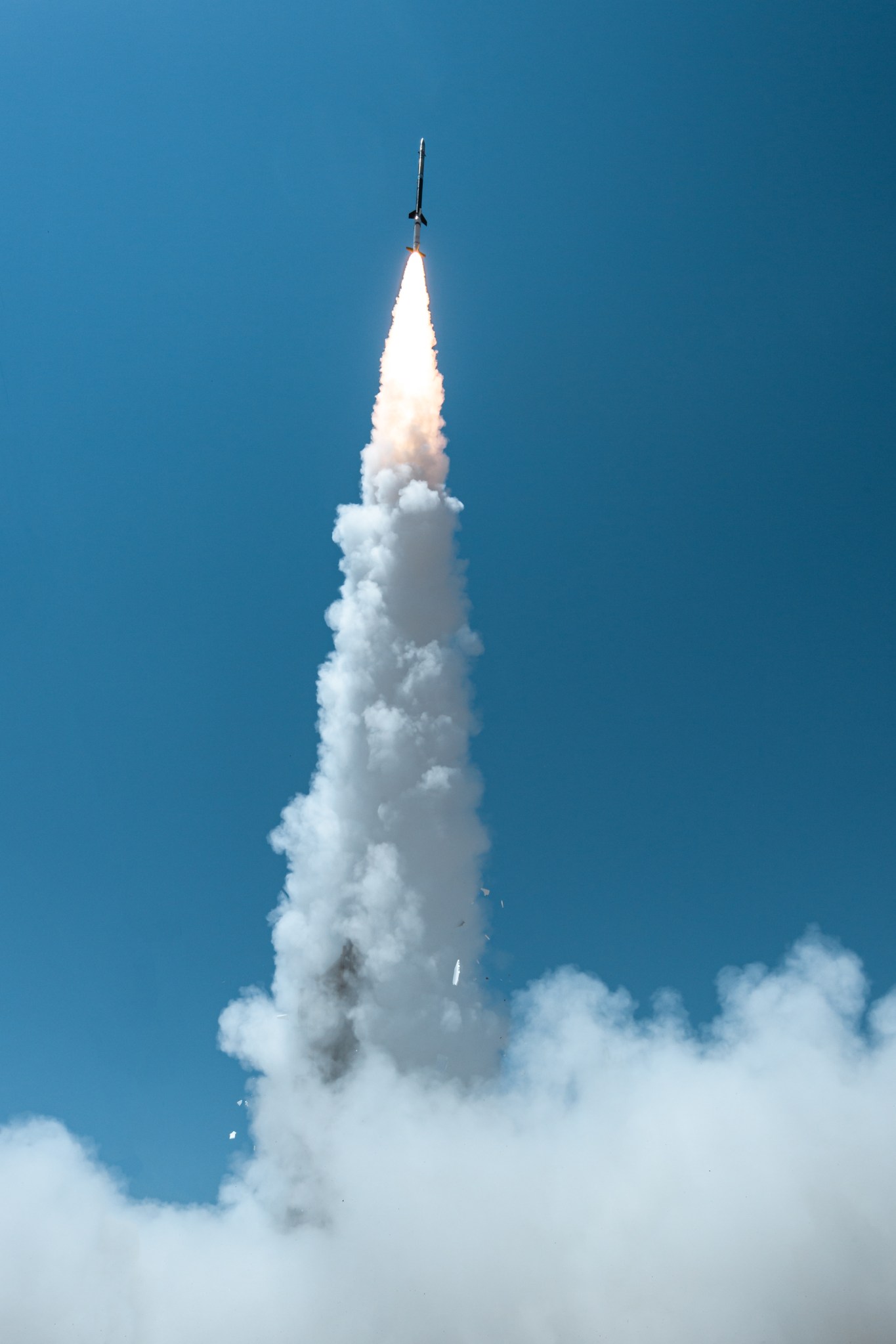 A sounding rocket launches into a bright blue sky leaving a plume of smoke behind.