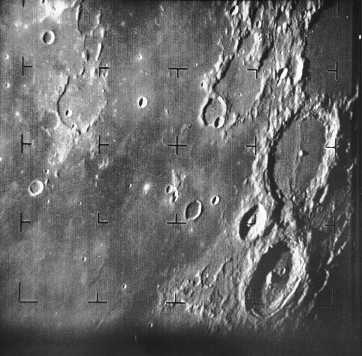 A black and white image of the Moon's surface. Many craters of different sizes can be seen. There is a grid of marks overlaid on the photo.