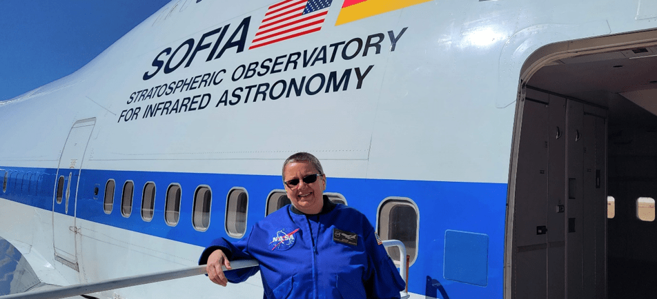 Diane Ripollone wearing a blue flight jacket standing in front of an SOFIA airplane