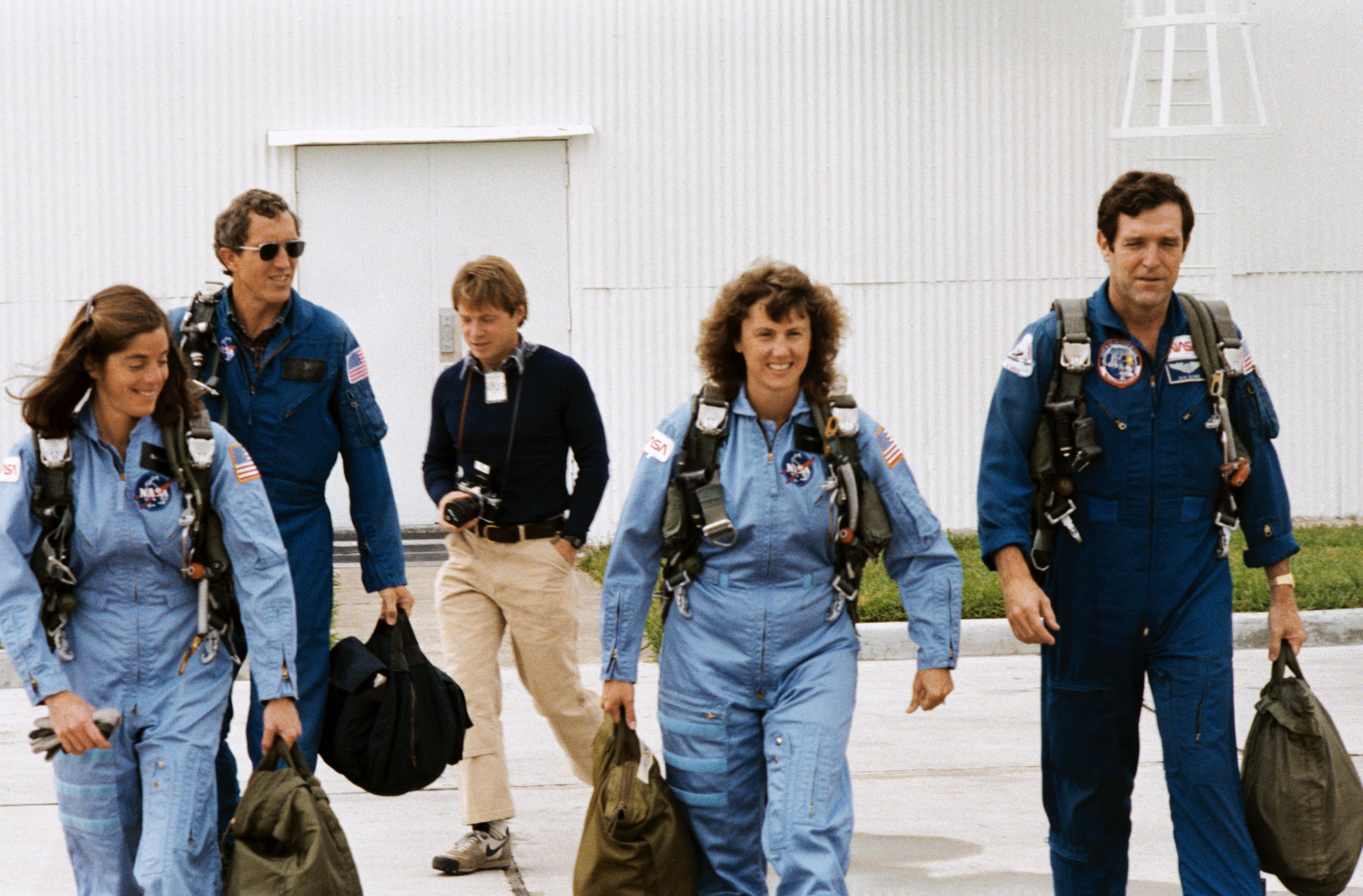 At Houston’s Ellington Air Force Base, Barbara R. Morgan, Michael J. Smith, a photographer, S. Christa McAuliffe, and Francis R. “Dick” Scobee walk onto the tarmac toward T-38 jet trainers