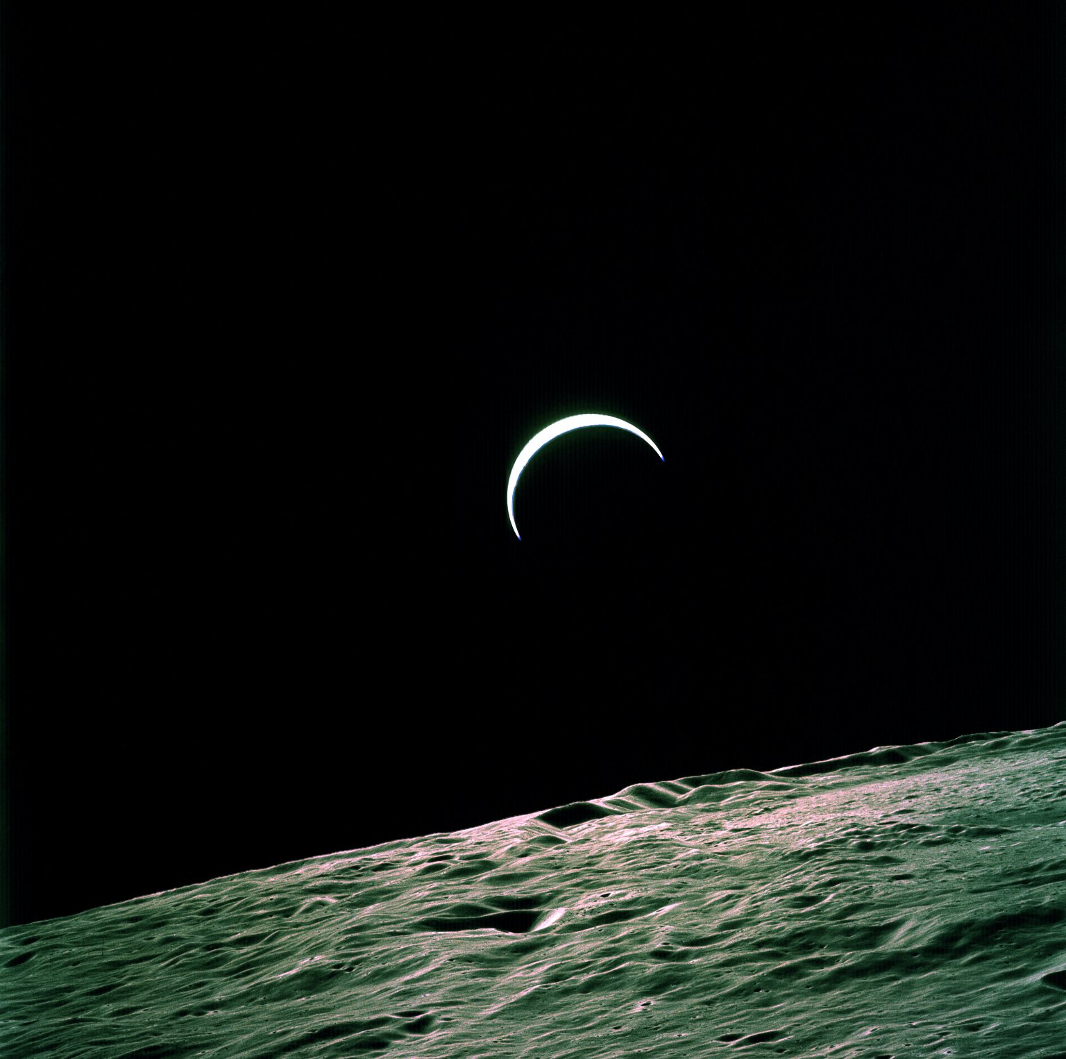 The Earth appears in the blackness of space as a slim white crescent. In the foreground is the rough, rocky gray surface of the Moon.