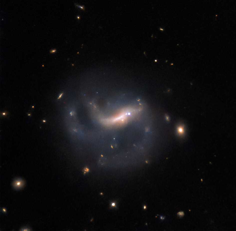 A close-in view of a barred spiral galaxy. A bright, glowing bar crosses the center of the galaxy, with blurred spiral arms curving away from its ends and continuing out of view. Bright points of light that indicate stars and background galaxies surround the featured barred spiral galaxy. The galaxy also hosts a bright supernova in its central bar, just right of image center.