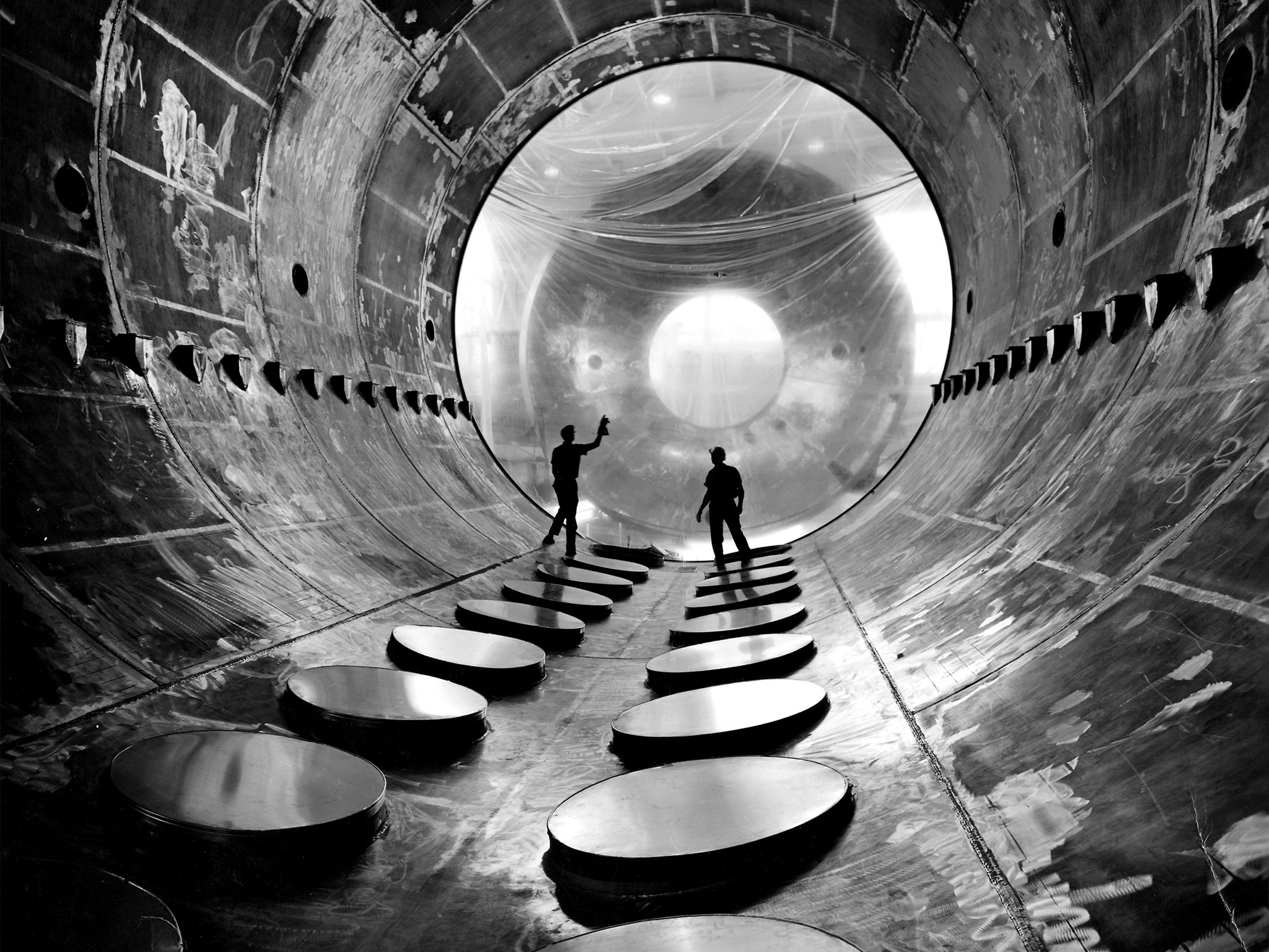 Two workers in a large vacuum tank.