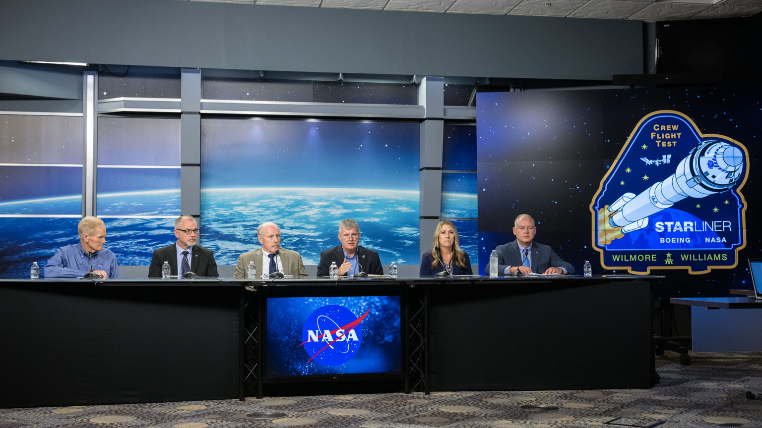 A group of NASA leaders sit at a table to conduct a live news conference at NASA Johnson.