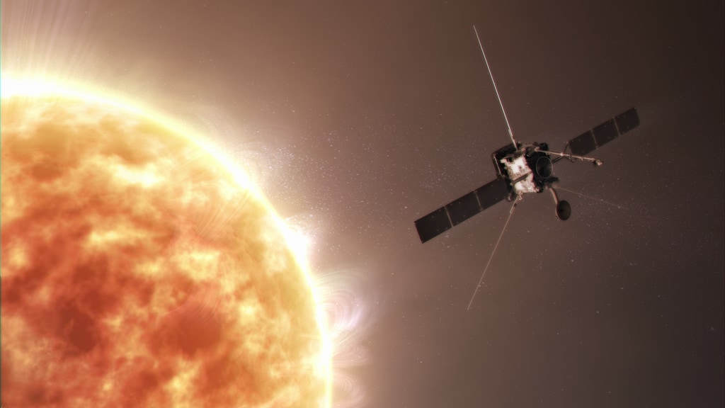 A portion of the Sun fills most of the left side of the image. On the right against the backdrop of space is Solar Orbiter with two long, black solar panels protruding from each side of the silver, box-shaped spacecraft and thin radio antennas attached to the top, back, bottom left, and bottom right of the spacecraft.