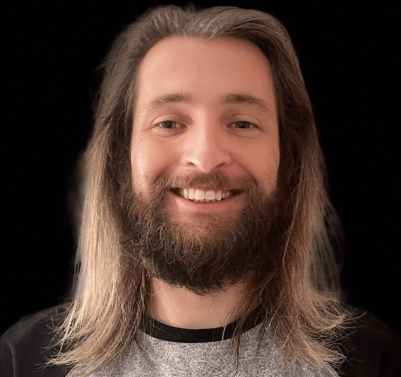 A man with long hair and a beard is smiling. His name is Drew Miles and he is a scientist.