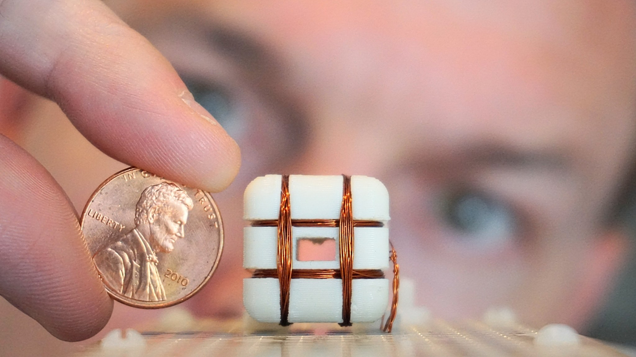 Close up image of a 3D printed plastic fixture wrapped with copper wire next to a penny.