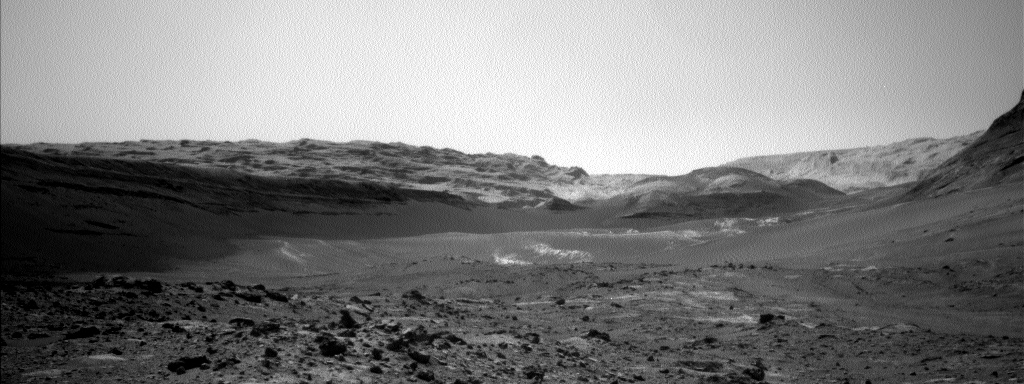 A grayscale photograph of the Martian surface shows rough, rocky terrain in the foreground and rolling hills and smooth dunes in the background.