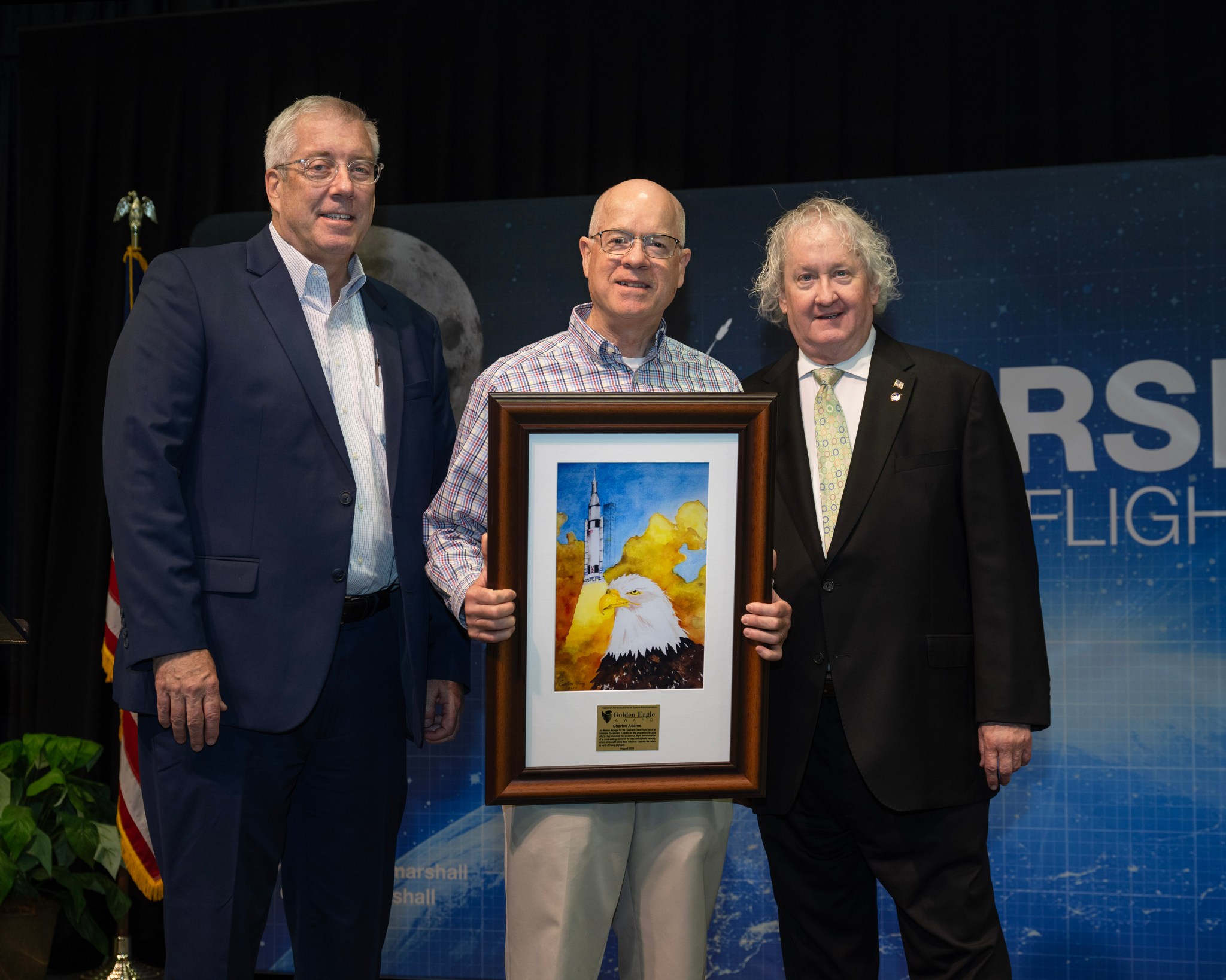 Charlie Adams, center, of Jacobs Space Exploration Group, displays the Golden Eagle Award presented to him during the Shared Experiences Forum. He is joined by Haars, left, and Hill, right.