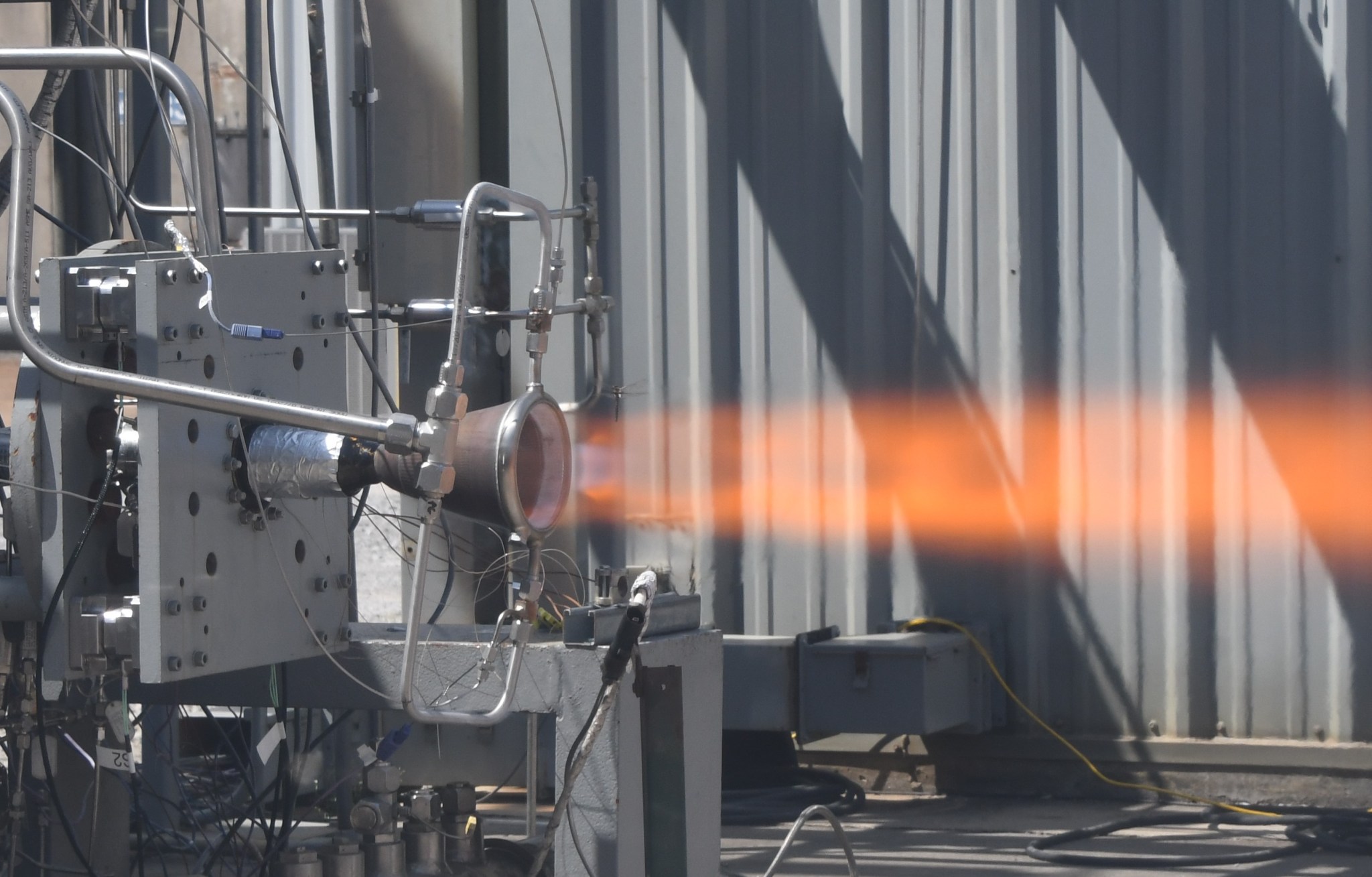 A hot fire test shows an orange flame coming out of a 3D printed chamber.