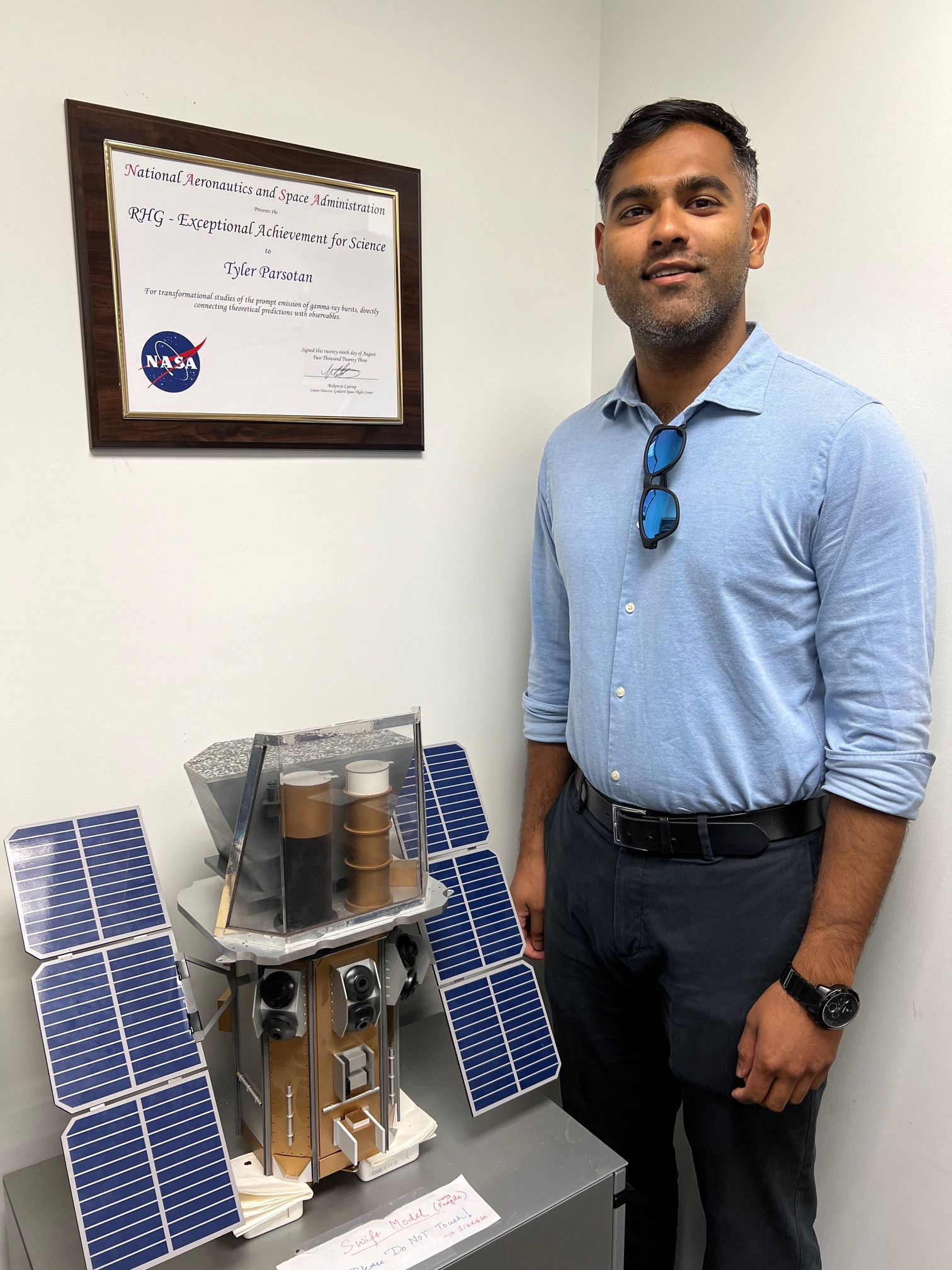 Man stands next to spacecraft model and his Robert H. Goddard Award for Exceptional Achievement for Science. He wears a blue button-down shirt and black pants.