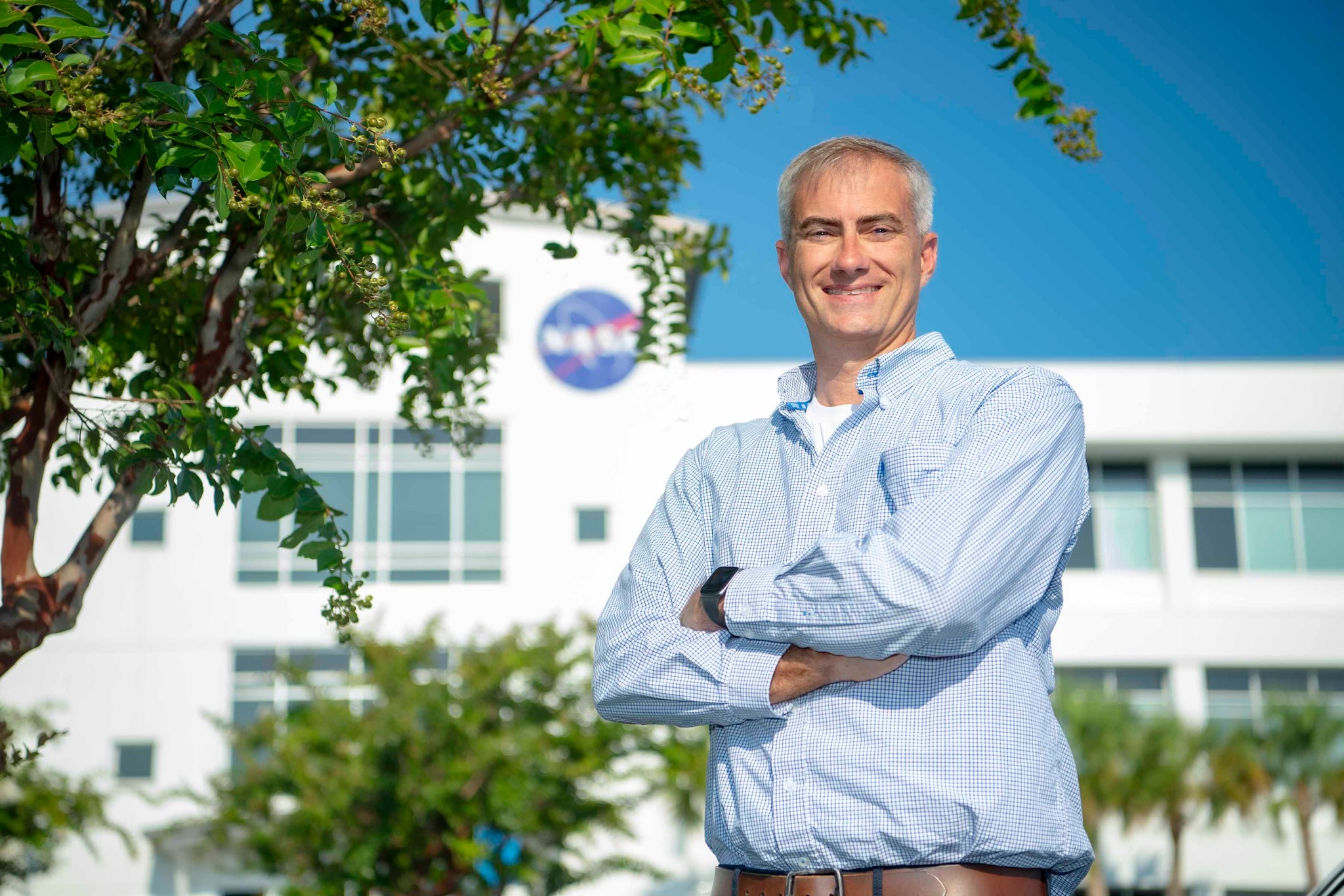 Joseph Ladner stands with his arms crossed under a tree in front of building at Stennis Space Center