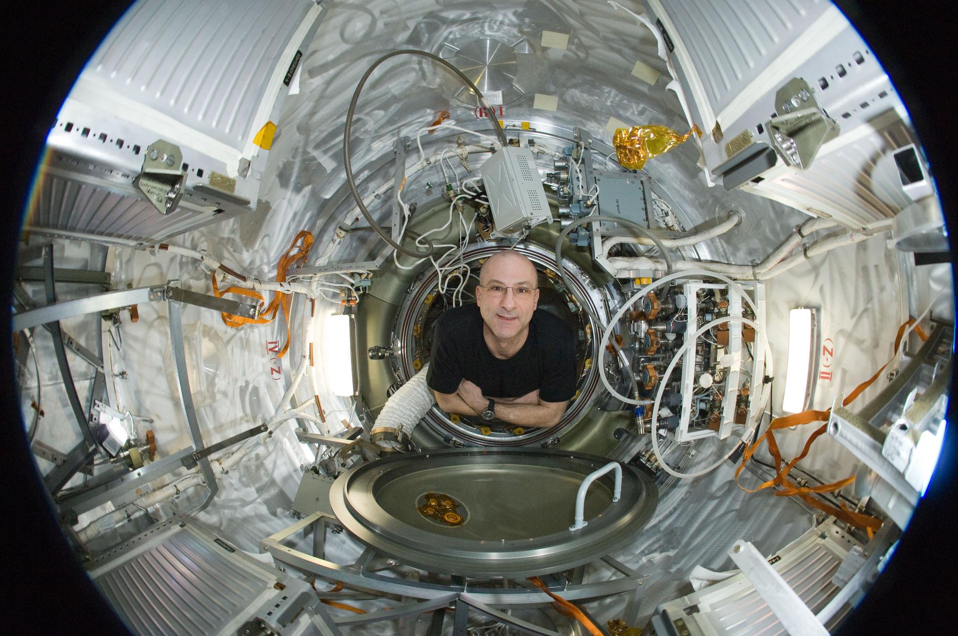 Don Pettit is floating in space station, arms folded, looking up at the camera.