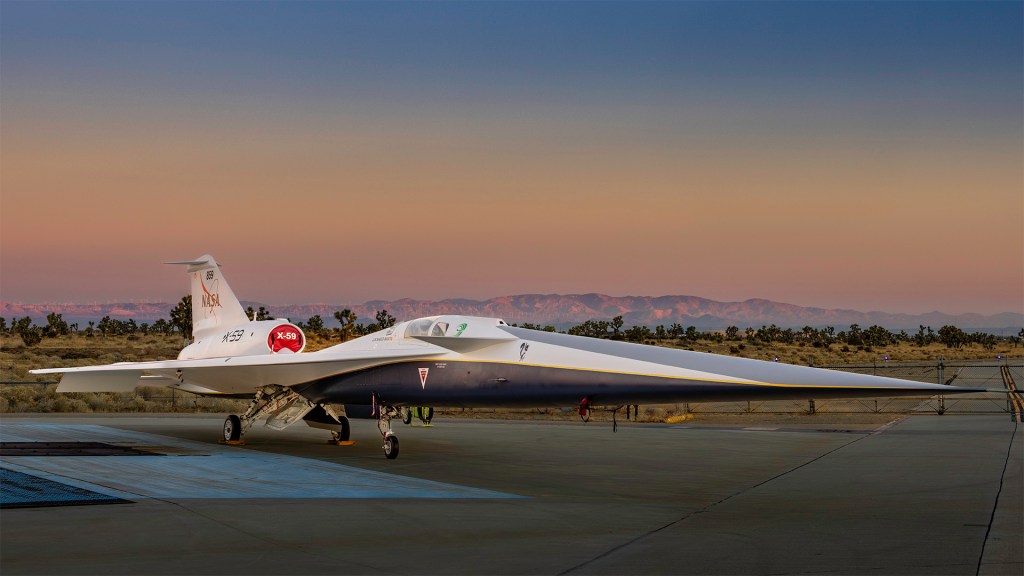 The X-59 sits on a runway with a sunset and moutains in the background.